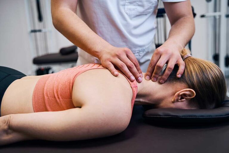 Athlete performing a guided balance exercise beside a treatment table in a bright rehabilitation room.